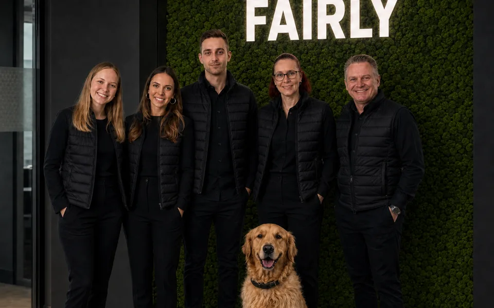 Das Fairly-Team mit Bürohund vor der Logowand